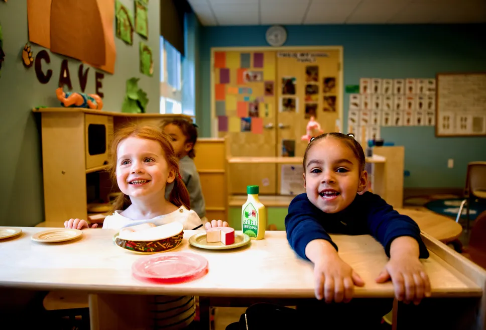 Two children playing with a wooden kitchen set with plastic plates and pretend food 