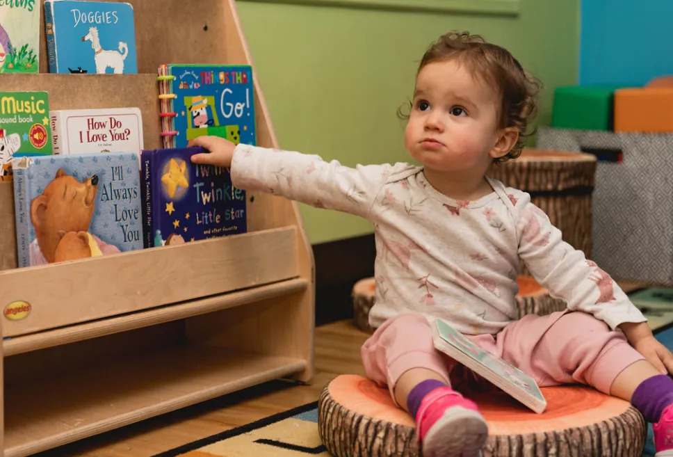 A child sitting on a nature-inspired cushion next to a bookshelf filled with age-appropriate books