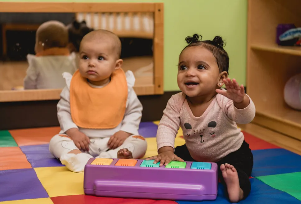 Two infants sitting and playing on a colorful play mat