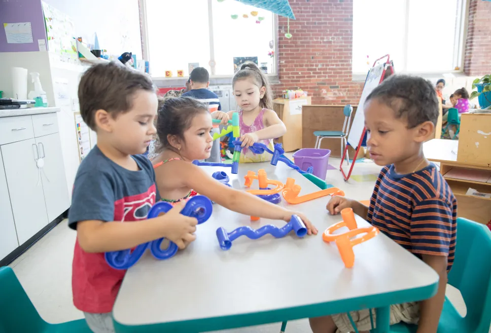 Three preschool students taking part in table play with plastic building pieces 