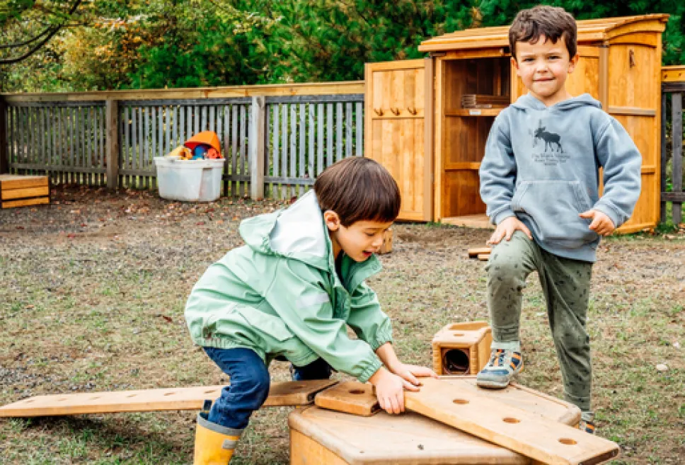 Two children using wooden building blocks in the secure outdoor playground