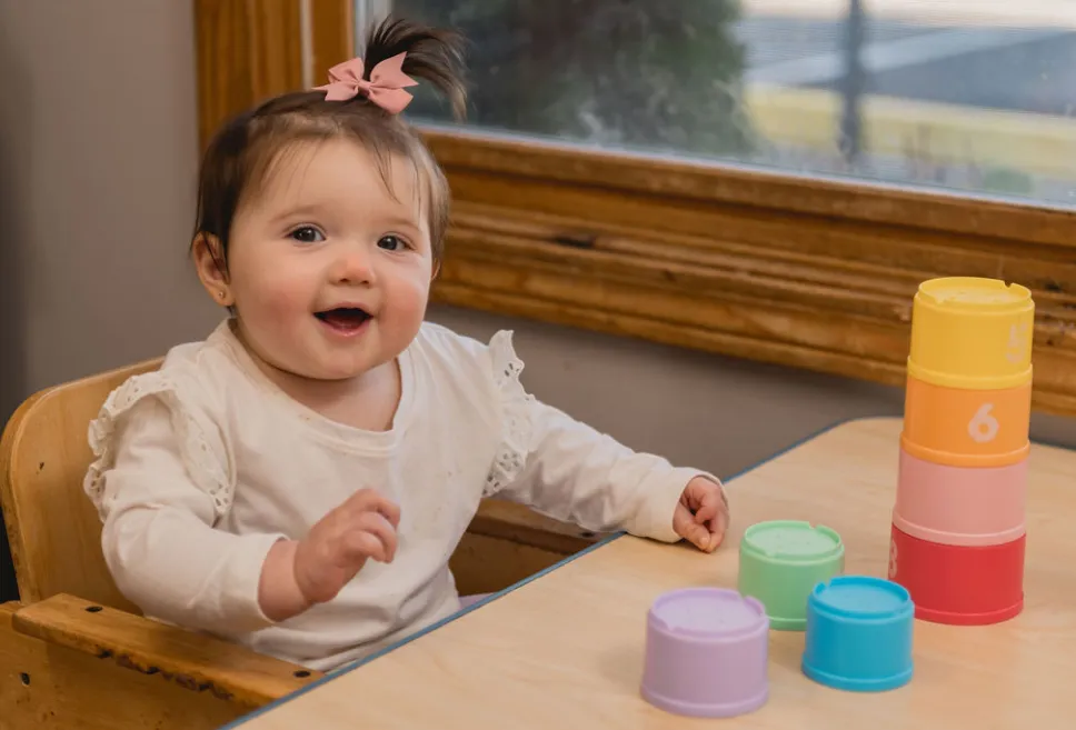 Infant with a pink bow in her hair playing with a colorful stacking tower