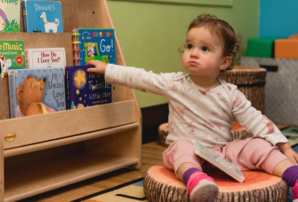 Infant sitting next to a bookshelf filled with children's books