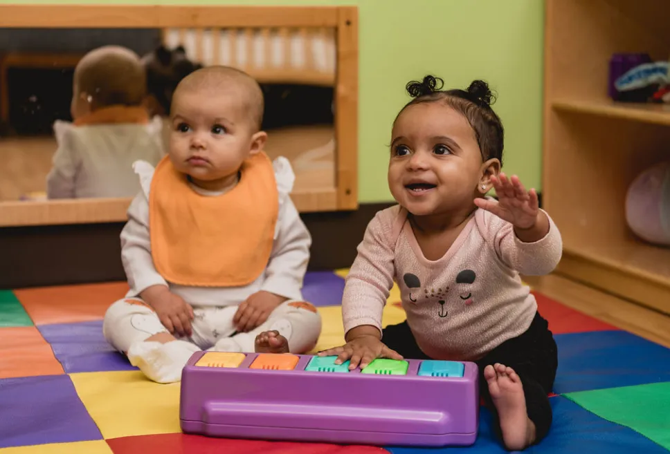 Two infants sitting and playing on a colorful play mat