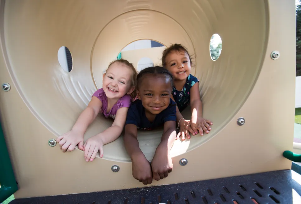 Three toddler friends playing in a tube on an outdoor playscape 