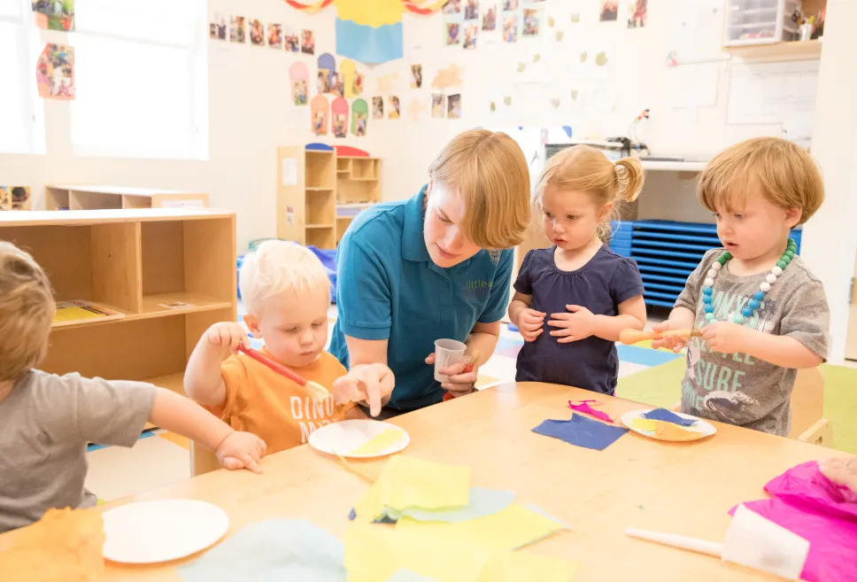 A teacher at a table instructing four toddlers 