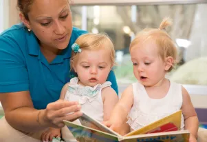 A teacher in a blue shirt reading to two children