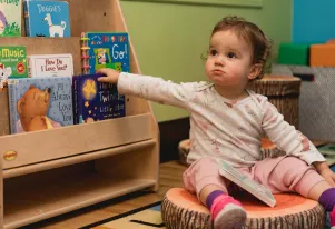 Infant sitting next to a bookshelf filled with children's books