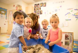 A teacher working four toddlers using a sensory box