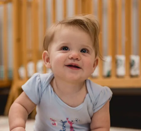 Smiling infant sitting while holding a wooden toy