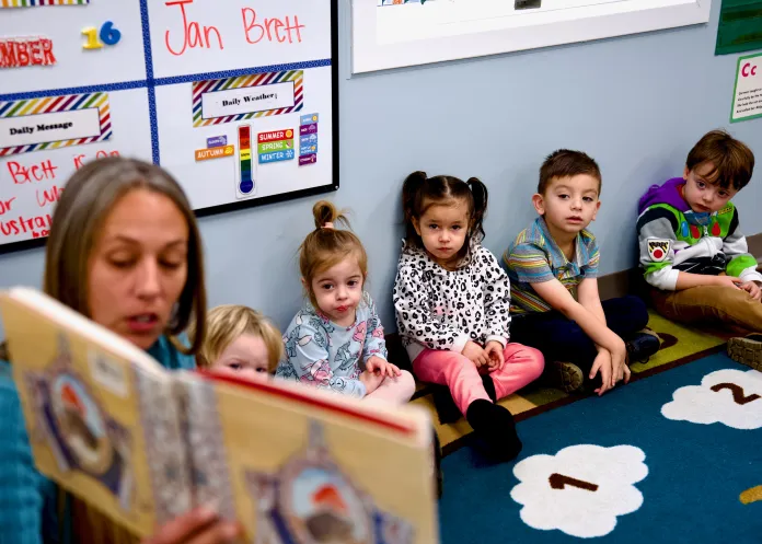 A teacher sitting on the floor reading a book to her classroom of five students
