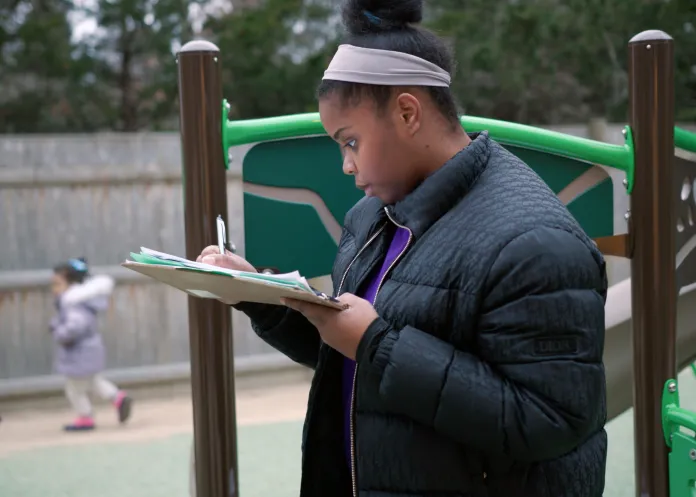 Teacher checking her clipboard while supervising students in the secure outdoor playground