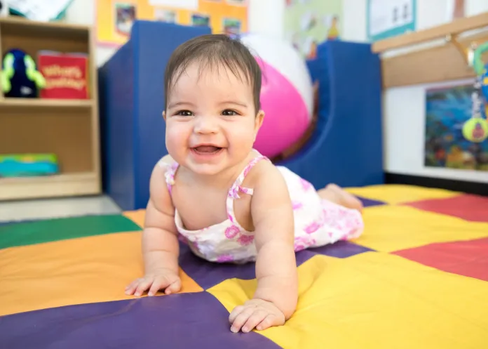 A smiling baby crawling across a yellow, purple, green, and red play mat