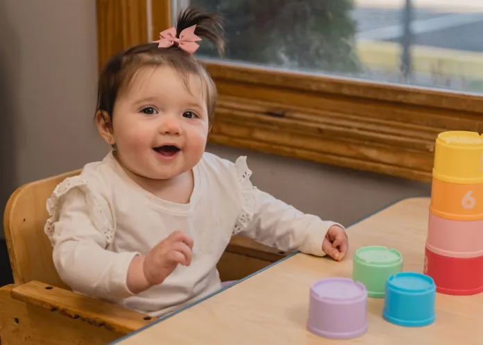 Child with a pink bow in her hair playing with a colorful stacking tower