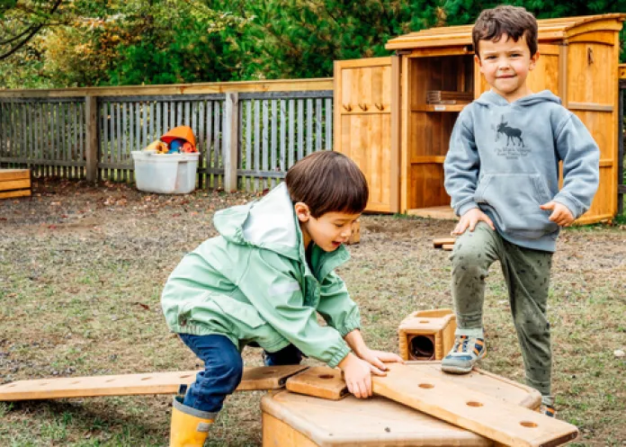 Two children using wooden building blocks in the secure outdoor playground