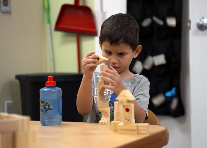 A child focused on stacking wooden blocks while taking part in play based learning