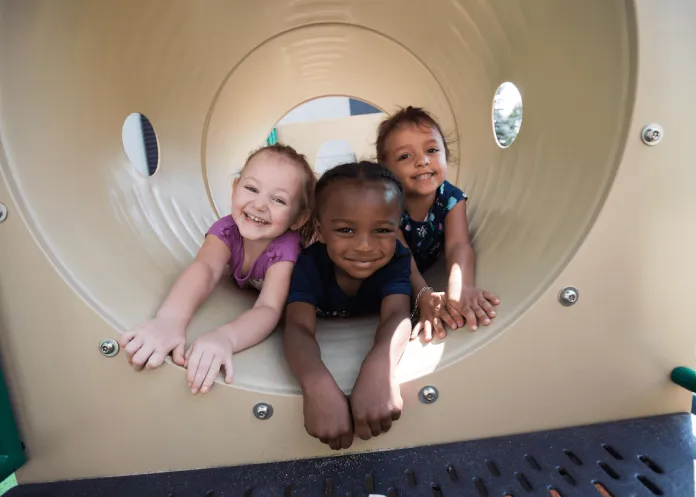 Three kids in Pre-K playing in a tunnel on a playground.
