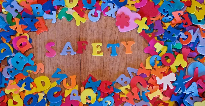 Safety spelled out in colorful letting on a wooden table surrounded by other colorful letters