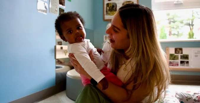 Teacher Holding a Baby in an infant classroom with light blue walls