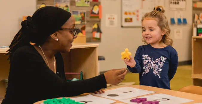 Preschool student learning to count with their teacher using numbers and colorful person shaped blocks