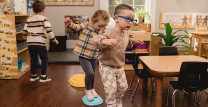 Two children walking on colorful stepping stones in the classroom