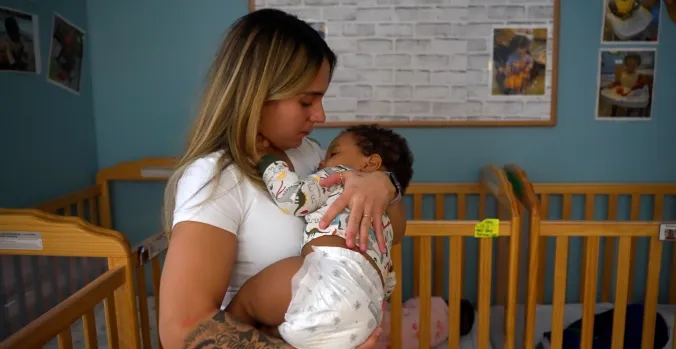 Teacher holding a sleeping baby with wooden cribs in the background
