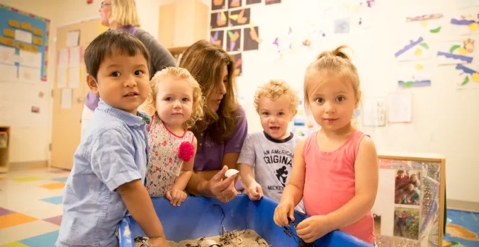 A teacher working four toddlers using a sensory box