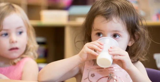 A toddler drinking milk from a clear plastic cup