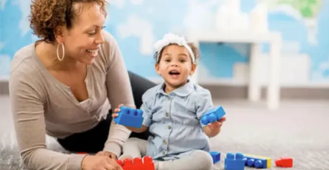 Parent and toddler smiling while playing with colorful building blocks